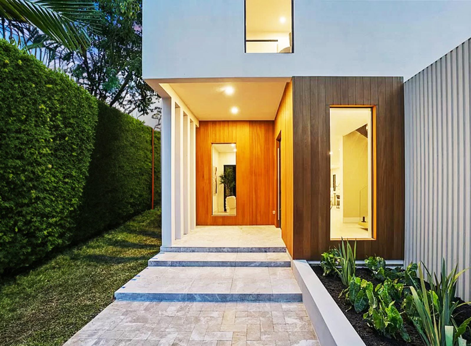 Entry sequence at the Wise Residence in Wilton Manors — warm wood surround and travertine steps framed by tropical planting